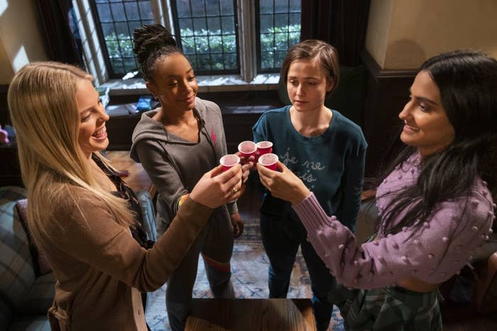 Four female college freshmen "cheers" with shot glasses. Three are happy. One in the middle looks apprehensive.