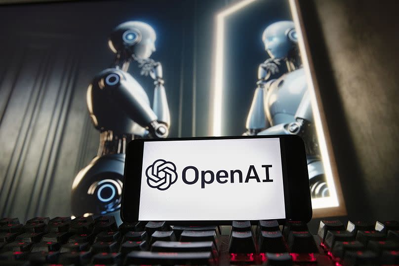 The OpenAI logo is seen displayed on a mobile phone with an image on a computer monitor generated by ChatGPT's Dall-E text-to-image model, Friday, 8 December 2023.