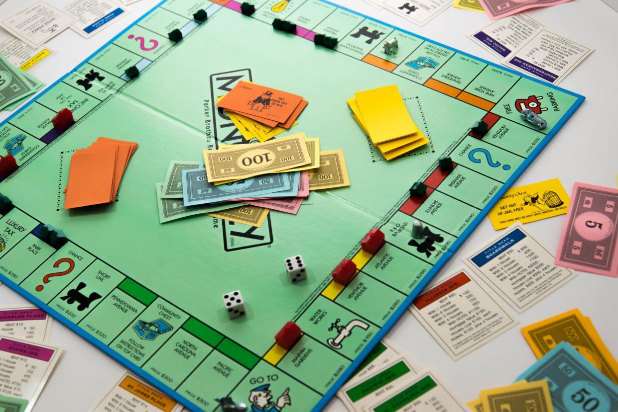 Monopoly board game in the middle of a game, paper money, cards, dice, and pieces during a game, players on all four sides, on a white sheet