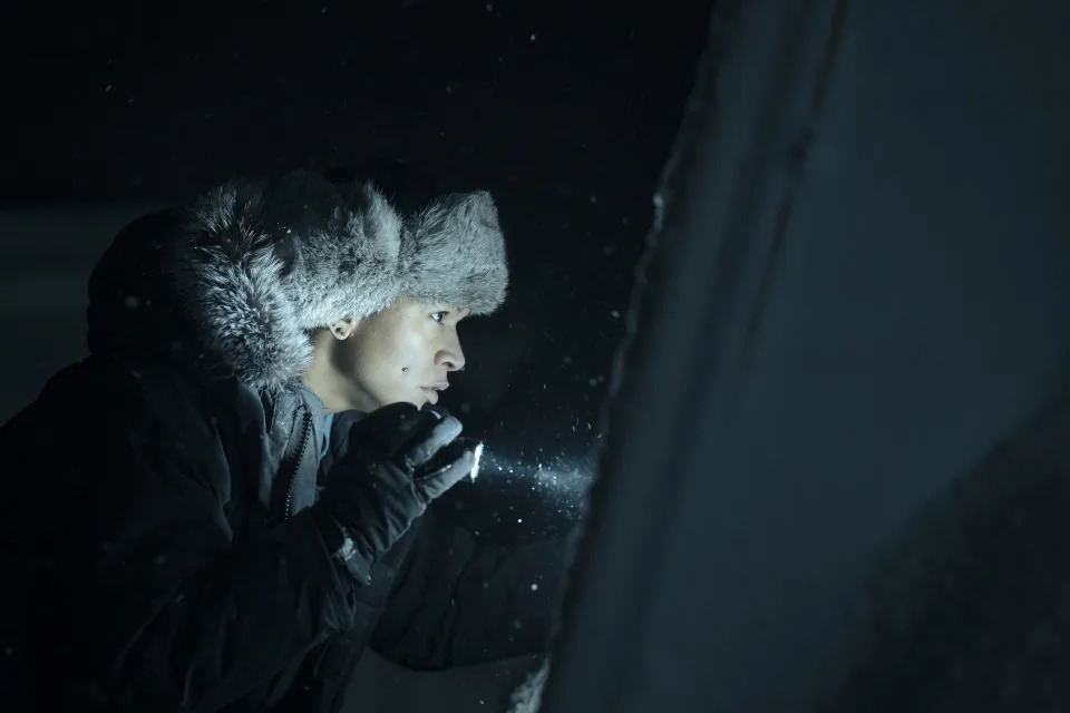 Kali Reis as Detective Navarro peers at something out of frame with a flashlight as snow falls around her in "True Detective: Night Country" 