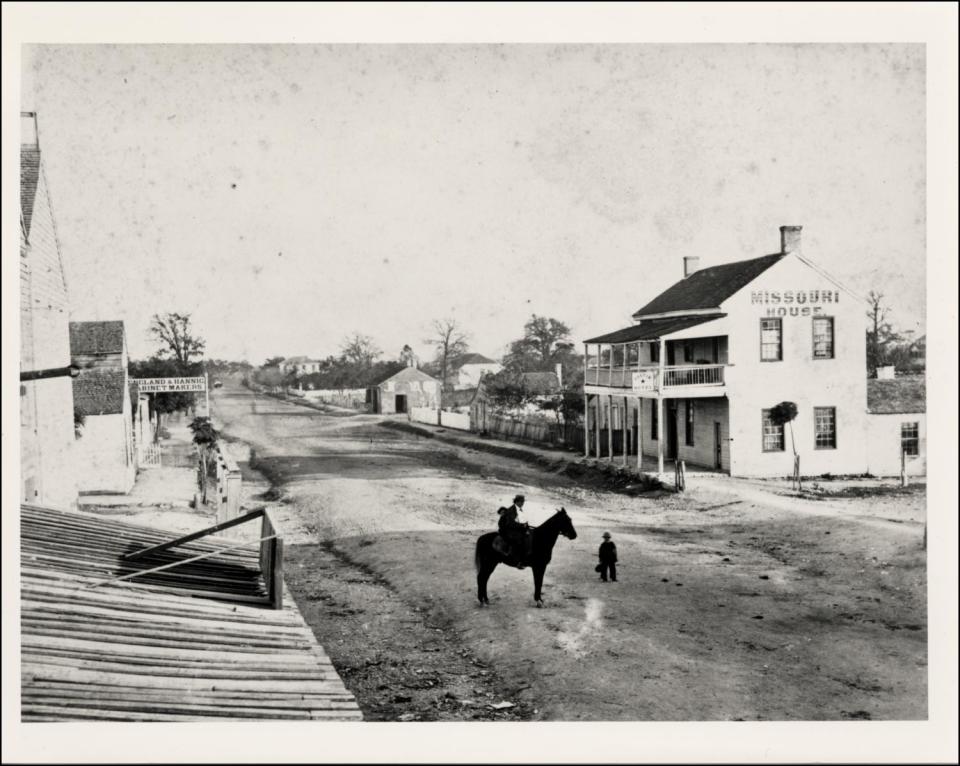 Photograph of 200 East Sixth Street circa 1866. The man on horse is William Oliphant who owned a jewelry store on Pecan Street in 1852. The child with him is Will Carter.
