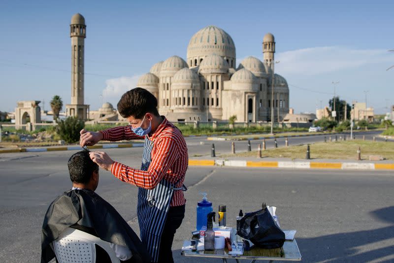 FILE PHOTO: A barber wearing a protective face mask cuts the hair of a policeman near the old bridge in the old city of Mosul