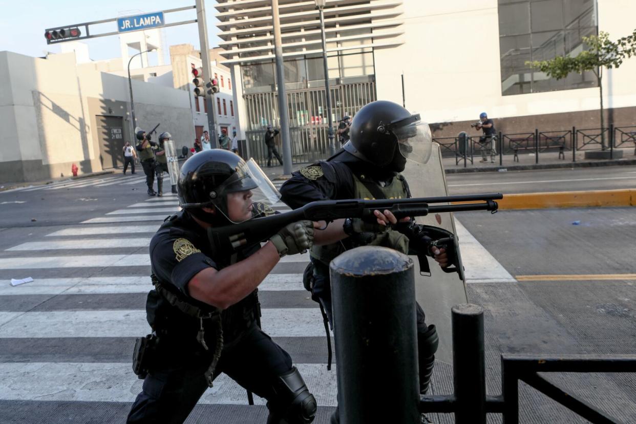 Police aim guns down a blocked off road in Lima, Peru.