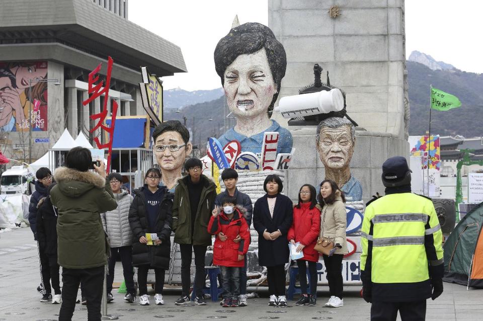 People pose for photos in front of effigies of impeached South Korean President Park Geun-hye, center, Hyundai Motor Co. Chairman Chung Mong-koo and Samsung Electronics Co. Vice Chairman Lee Jae-yong, left, in Seoul, South Korea, Thursday, Jan. 5, 2017. South Korean lawmakers on Thursday accused Park of "broadly and gravely" violating the constitution as the country's Constitutional Court began hearing oral arguments in her impeachment trial. (AP Photo/Ahn Young-joon)