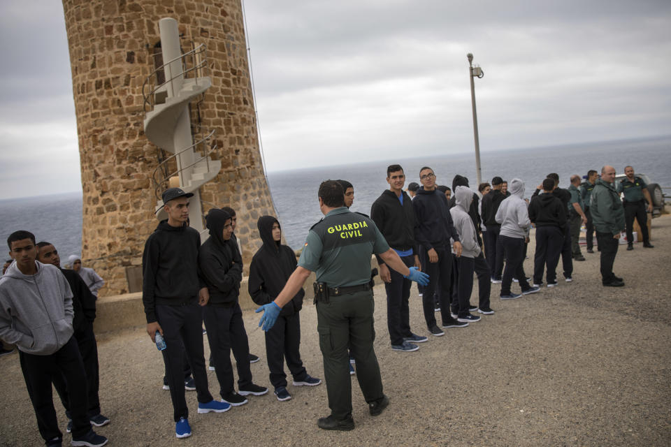 FILE - In this June. 28, 2018 file photo, a Guardia Civil officer stands next to Moroccan migrants after they arrived on the beach sailing on a rubber dinghy near Tarifa, in the south of Spain. Spain appears to have stemmed a surge in illegal migration that made it the main Mediterranean entry point for migrants seeking ways into Europe by increasing Morocco's involvement in border control. (AP Photo/Emilio Morenatti, File)