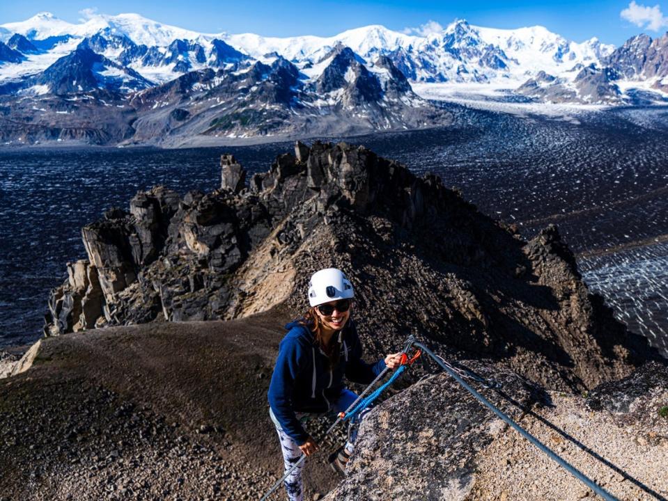 Woman climbing down mountain in Alaska with blue, white-capped mountains in the background