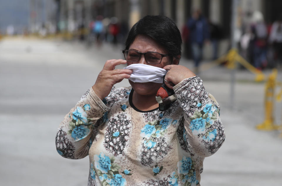 A woman hurriedly places a protective face mask over her mouth and nose to avoid a $100.00 US dollar fine, as wearing a face mask in public is mandatory, in Quito, Ecuador, Wednesday, June 10, 2020. The city is returning to a new normality after relaxing a rigorous quarantine but amid a certain fear that new coronavirus infections may rise. (AP Photo/Dolores Ochoa)