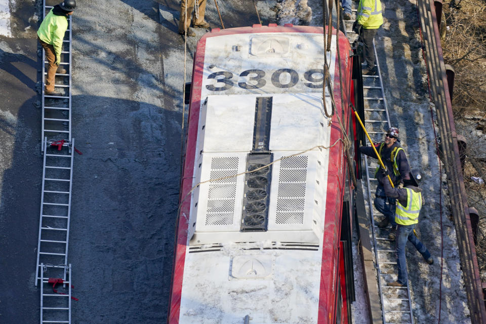 Workers use use a pole to reach for a hoisting strap from ladders placed along the sides of the bus that was on a bridge when it collapsed Friday as they work to remove it during the recovery process on Monday Jan. 31, 2022 in Pittsburgh's East End. (AP Photo/Gene J. Puskar)