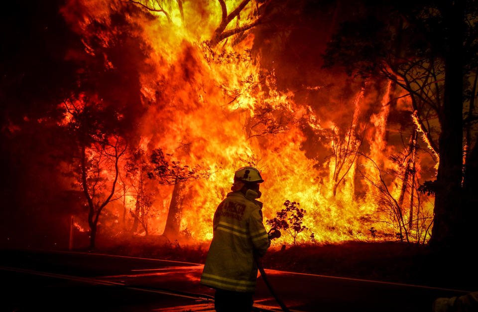 Fire and Rescue personnel prepare to use a hose in an effort to extinguish a bushfire as it burns near homes on the outskirts of the town of Bilpin.