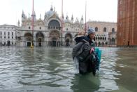 FILE PHOTO: A woman carrying a child on her back wades in the flooded St. Mark's Square in Venice, Italy