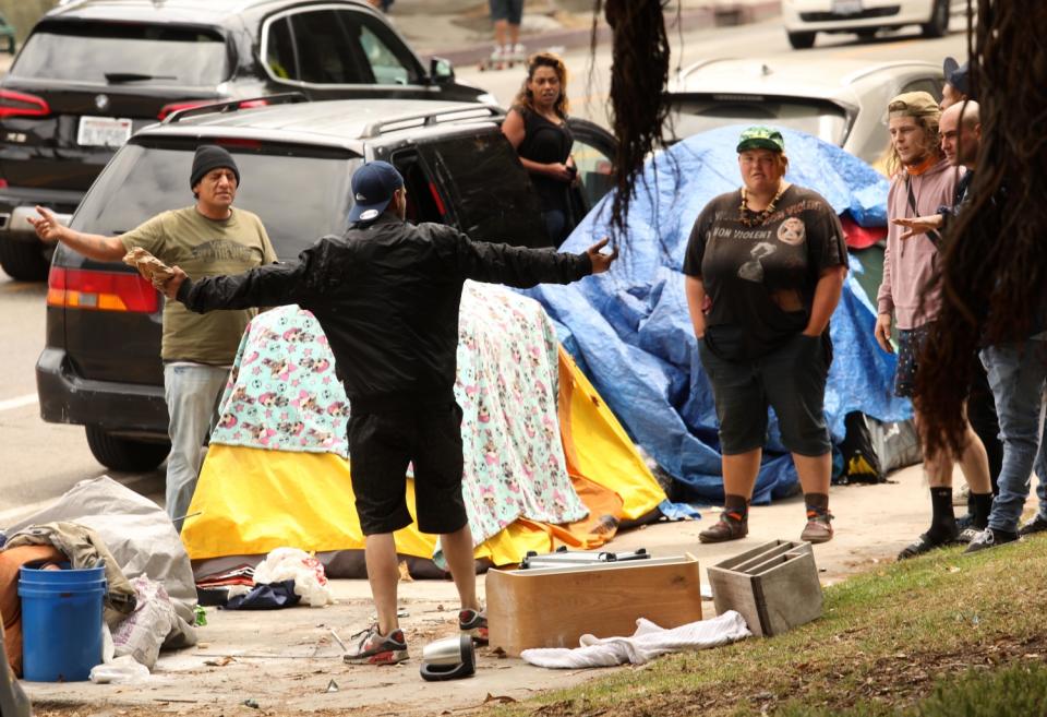 A man stands with his arms out as other people confront him near tents