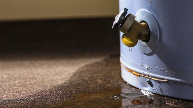 Water leaking from the plastic faucet on a residential electric water heater sitting on a concrete floor.