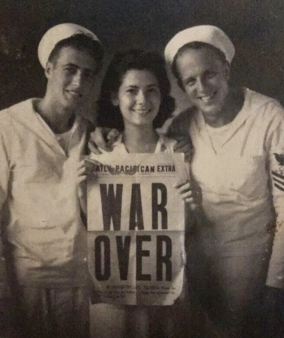 A woman holding a "War Over" newspaper next to two soldiers