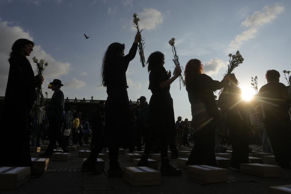 Women hold flowers and walk among boxes representing symbolic coffins as they remember former guerrillas and social leaders who have been killed since the 2016 signing of a peace agreement between rebels of the Revolutionary Armed Forces of Colombia, FARC, and the government, in Bogota, Colombia, Tuesday, Feb. 20, 2024. (AP Photo/Fernando Vergara)