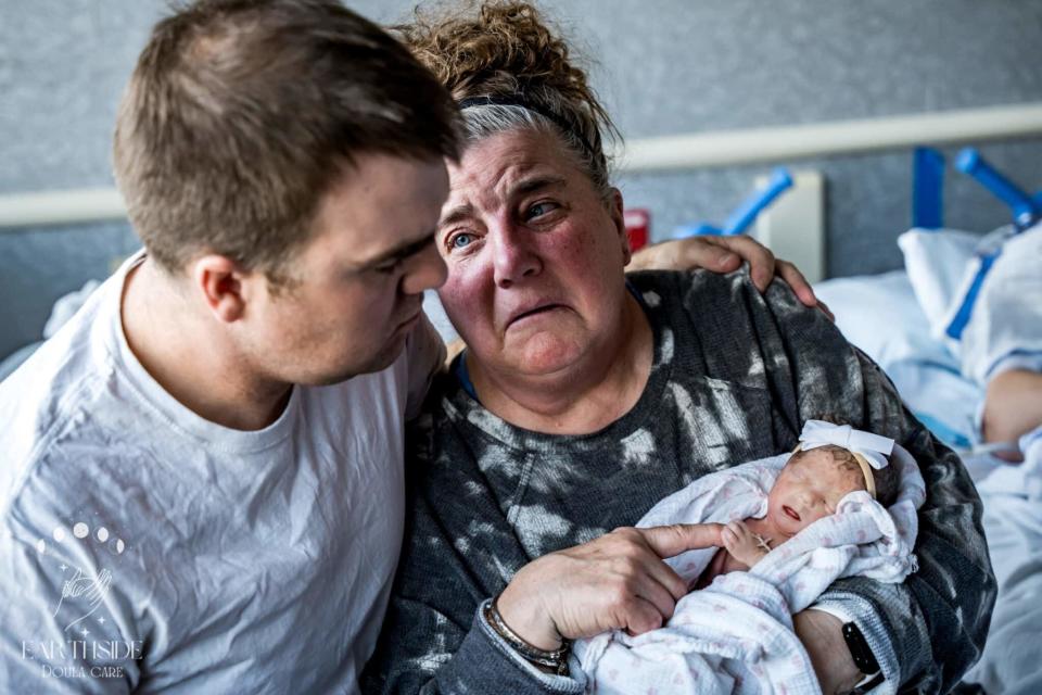 Two adults appear emotional holding a newborn born still; they're sitting on a hospital bed