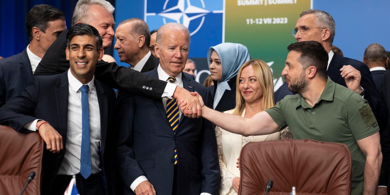 Ukraine's President Volodymyr Zelenskyy, right, reaches past US President Joe Biden to shake hands with Lithuania's President Gitanas Nauseda as they stand with other NATO members, including British Prime Minister Rishi Sunak, left, at the NATO Summit in Vilnius, Lithuania