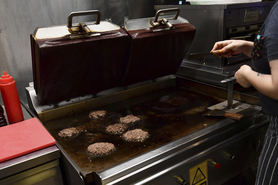 A worker cooks burgers at Zing Burger store in Budapest, Hungary, Monday, Sept. 12, 2022. Richard Kovacs, a business development manager for the Hungarian burger chain, said some of the chain's 15 stores have seen a 750% increase in electricity bills since the beginning of the year – leading to additional monthly costs of up to 1.5 million Hungarian forints ($3,840) per store. (AP Photo/Anna Szilagyi)