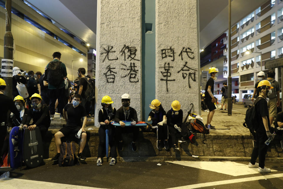 Protesters rest near graffiti which reads "Recovery of Hong Kong, An Era Revolution" in Hong Kong on Sunday, July 21, 2019. Protesters in Hong Kong pressed on Sunday past the designated end point for a march in which tens of thousands repeated demands for direct elections in the Chinese territory and an independent investigation into police tactics used in previous demonstrations. (AP Photo/Vincent Yu)