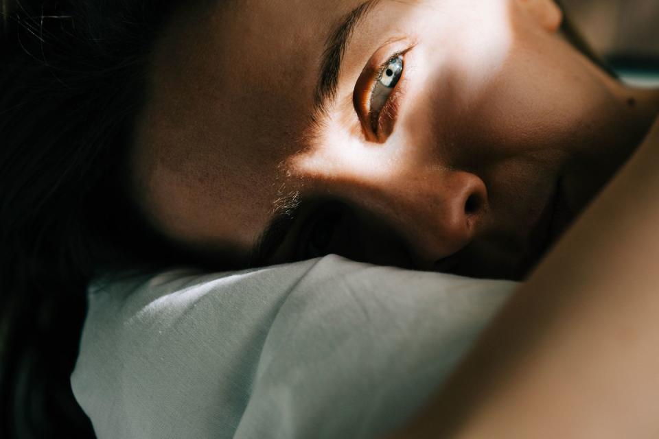 sleepless woman lying in bed hiding under duvet