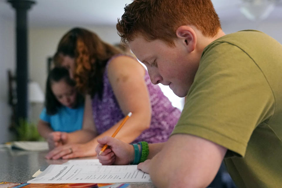 Noah Osgood, 12, right, works on a review sheet as his mother, Jennifer, helps his sister, Lily, at their home in Fairfax, Vt., on Tuesday, July 20, 2021. “He told me he was learning so much more at home than he ever did in school,’’ Jennifer says. “He said, ‘School is just so chaotic -- we don’t get very much done in any particular class. Here, I sit down, you tell me what to do, and minutes later I’m done.'” (AP Photo/Charles Krupa)