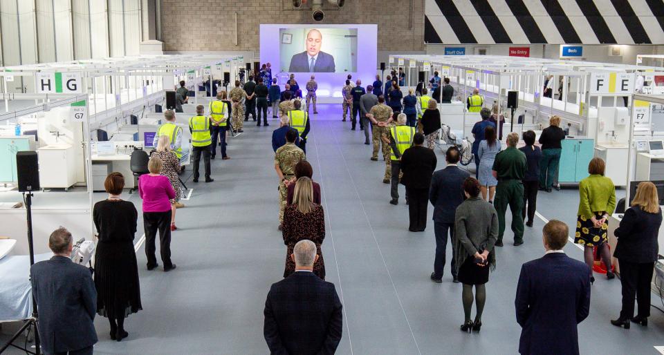 People observe social distancing measures as they stand amongst Hospital cubicles, as a giant screen displays an image of Britain's Prince William, Duke of Cambridge, as he speaks via video-link during the official opening of the NHS Nightingale Hospital Birmingham, setup inside the National Exhibition Centre (NEC) in Birmingham, central England on April 16, 2020, to help Britain's National Health Service cope with an expected influx of patients during the novel coronavrius pandemic. - The British government was on Thursday expected to extend a nationwide lockdown for another three weeks, amid signs the coronavirus outbreak is peaking, but warnings of more deaths to come. (Photo by Jacob King / POOL / AFP) (Photo by JACOB KING/POOL/AFP via Getty Images)