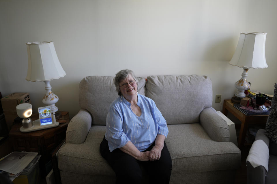 Joyce Loazia poses for a picture next to ElliQ, left, a tabletop device that uses artificial intelligence to conduct human-like conversations, during an interview in her apartment in a senior community in Coral Springs, Fla., Tuesday, Dec. 5, 2023. Loazia is among the first in the country to receive the robot ElliQ, whose creators, Intuition Robotics, and senior assistance officials say is the only device using artificial intelligence specifically designed to lessen the loneliness and isolation experienced by many older Americans. (AP Photo/Rebecca Blackwell)