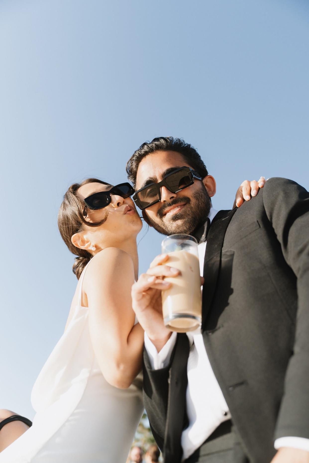 A bride and groom embrace wearing sunglasses.