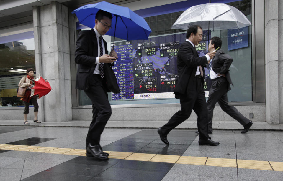 Men check their mobile phones as they walk by an electronic stock indicator in Tokyo Tuesday, May 15, 2012. Asian stock markets were mostly lower Tuesday, rattled by a political impasse in Greece that could lead the debt-stricken country to a destabilizing exit from the euro currency union. Japan's Nikkei 225 index fell 73.10 points, or 0.81 percent, to close at 8,900.74, a new three-month low. (AP Photo/Shizuo Kambayashi)