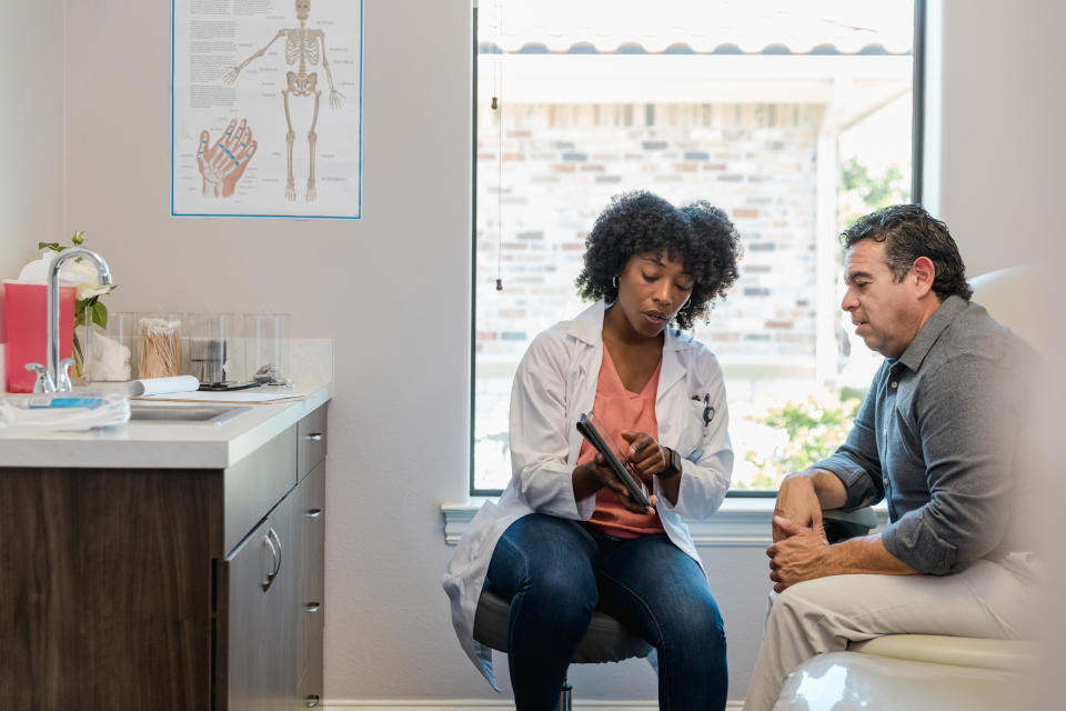 The mid adult female doctor points out something on the digital tablet as the mature adult male patient listens carefully.