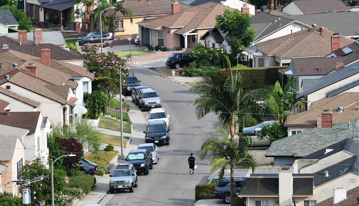 A lone man walks along a suburban street lined with vehicles. 