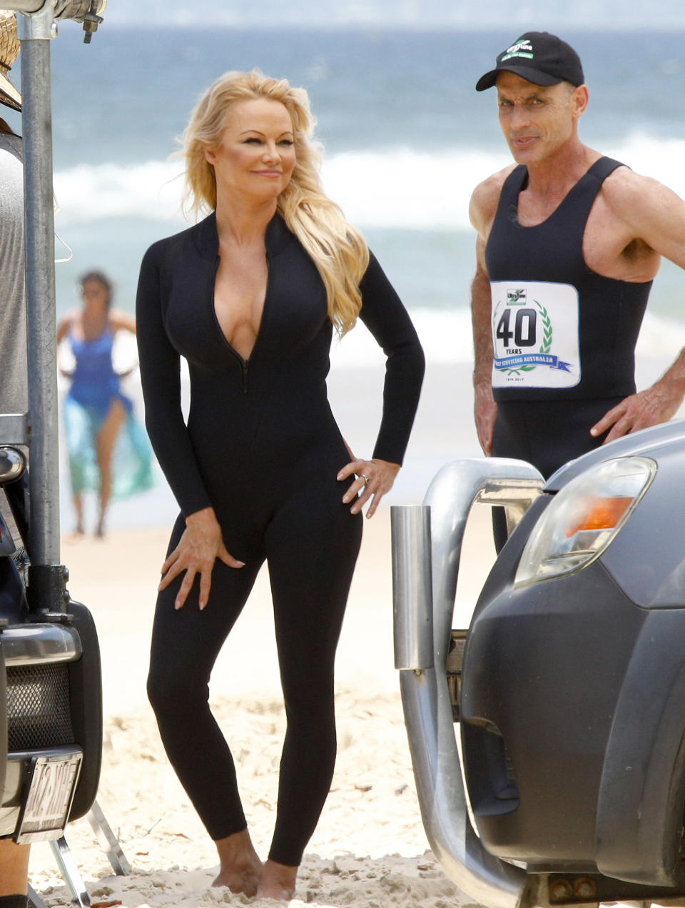 Pamela Anderson poses in a black wetsuit unzipped on set the Ultratune set on Gold Coast beach