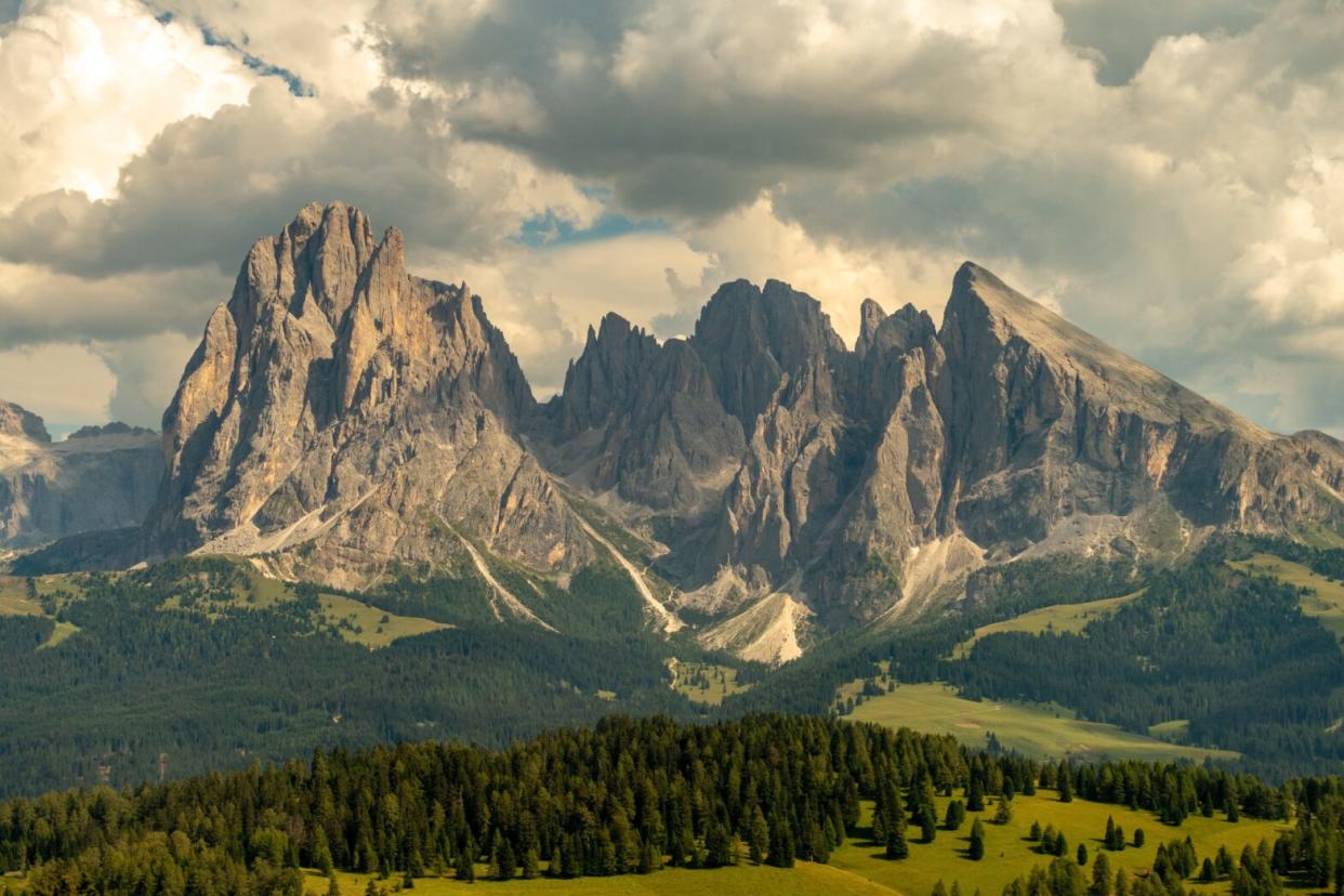 The Dolomites of Italy are a stunning mountain range that travelers should not miss. Pictured: The Italian Dolomites on a cloudy day with a green thriving forest