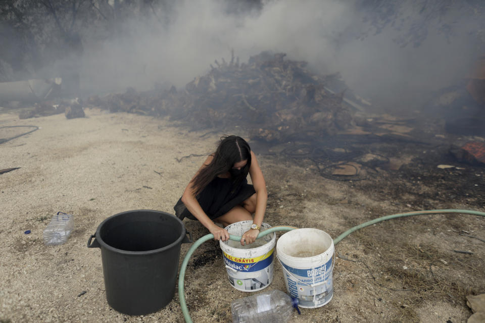 A young woman fills buckets with water for local residents trying to stop a forest fire from reaching their homes in the village of Figueiras, outside Leiria, central Portugal, Tuesday, July 12, 2022. Hundreds of firefighters in Portugal continue to battle fires in the center of the country that forced the evacuation of dozens of people from their homes mostly in villages around Santarem, Leiria and Pombal. (AP Photo/Joao Henriques)