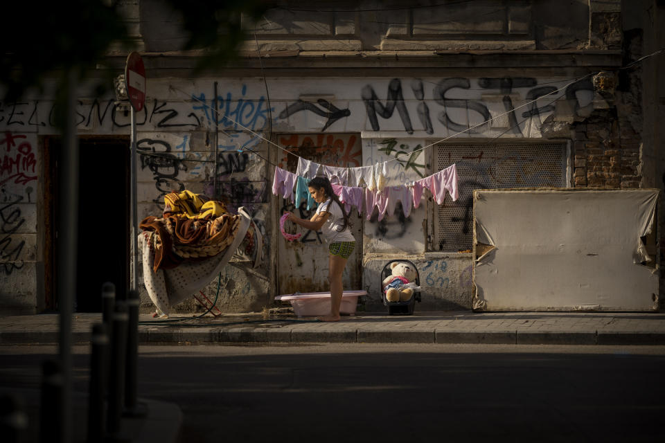 A child hangs baby clothing for drying, outside an old building in downtown Bucharest, Romania, Saturday, June 3, 2023. (AP Photo/Vadim Ghirda)