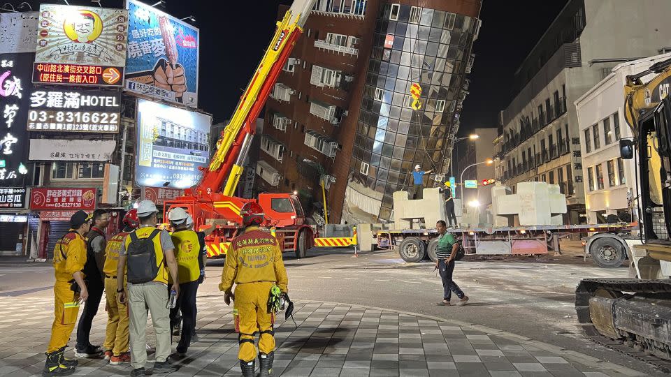 Rescue workers stand near the site of a leaning building in the aftermath of the earthquake. - Johnson Lai/AP