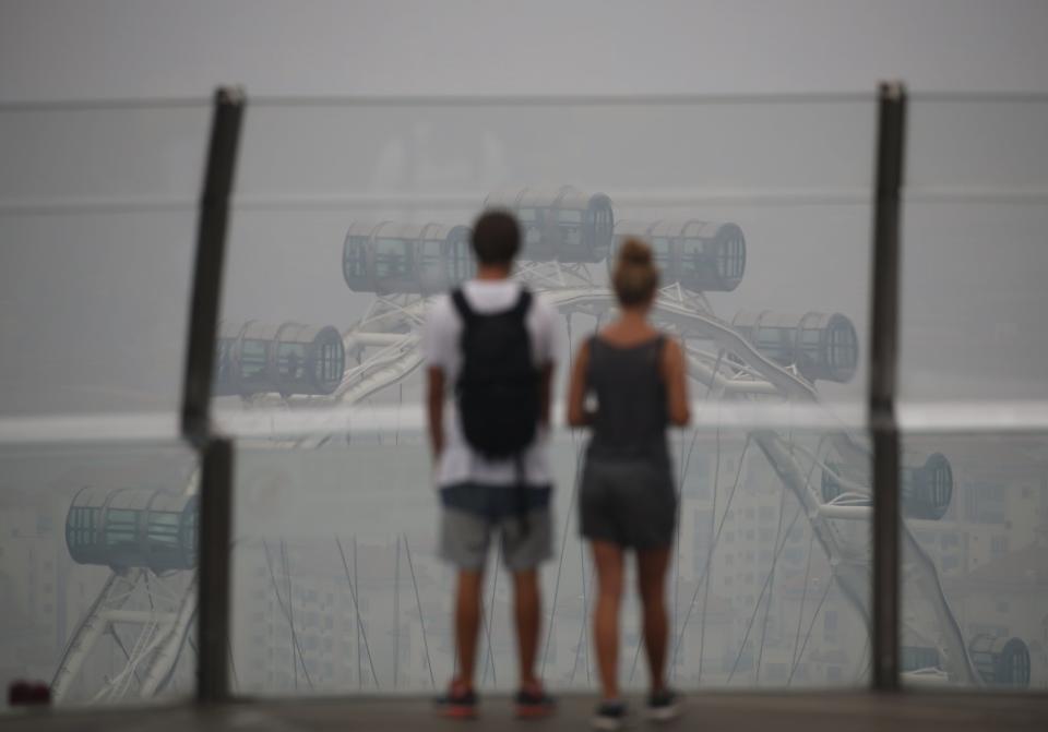 Tourists look at the Singapore Flyer observatory wheel shrouded by haze in Singapore