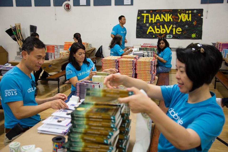 Five people wearing AbbVie t-shirts with books in a room with a thank-you poster in the background.