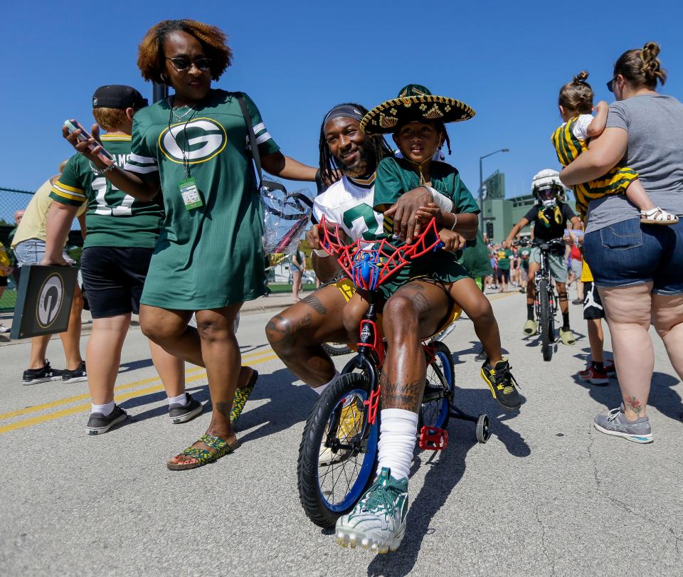 Green Bay Packers running back Aaron Jones carries his son, Aaron Jones, Jr., on his back as he rides a bicycle to practice on Saturday, July 29, at Ray Nitschke Field.