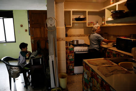 Housewife, Mariela Garzon cooks in the kitchen as a child look at a computer inside a flat on the 4th floor of an apartment block in Caracas, Venezuela, March 18, 2019. REUTERS/Carlos Jasso