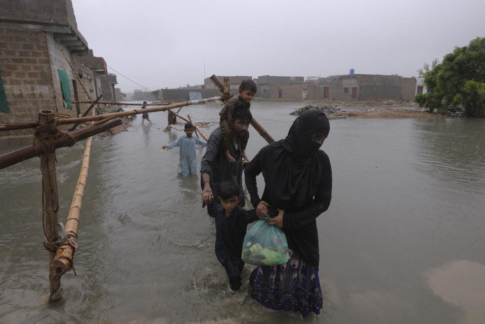 A family wade through a flooded area during a heavy monsoon rain in Yar Mohammad village near Karachi, Pakistan, Thursday, Aug. 27, 2020. Pakistan's military said it will deploy rescue helicopters to Karachi to transport some 200 families to safety after canal waters flooded the city amid monsoon rains. (AP Photo/Fareed Khan)