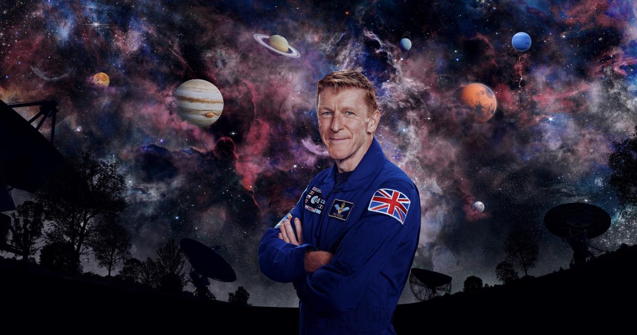  Tim Peake with his arms crossed standing in front of a galaxy background for Secrets of Our Universe with Tim Peake. 