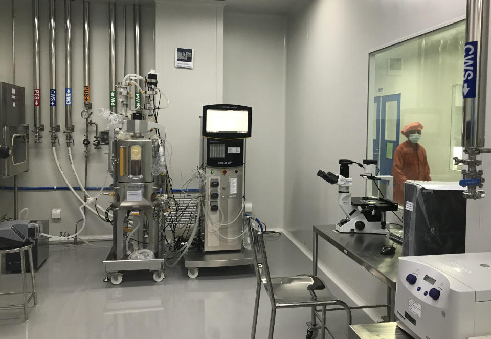 A member of production personnel walks in a corridor past a room containing a Disposable 50L Bioreactor (STR50) System with peristaltic pumps and an Inverted Microscope inside the Incepta plant on the outskirts of Dhaka in Bangladesh Saturday Feb. 13, 2021. (AP Photo/Al-emrun Garjon)