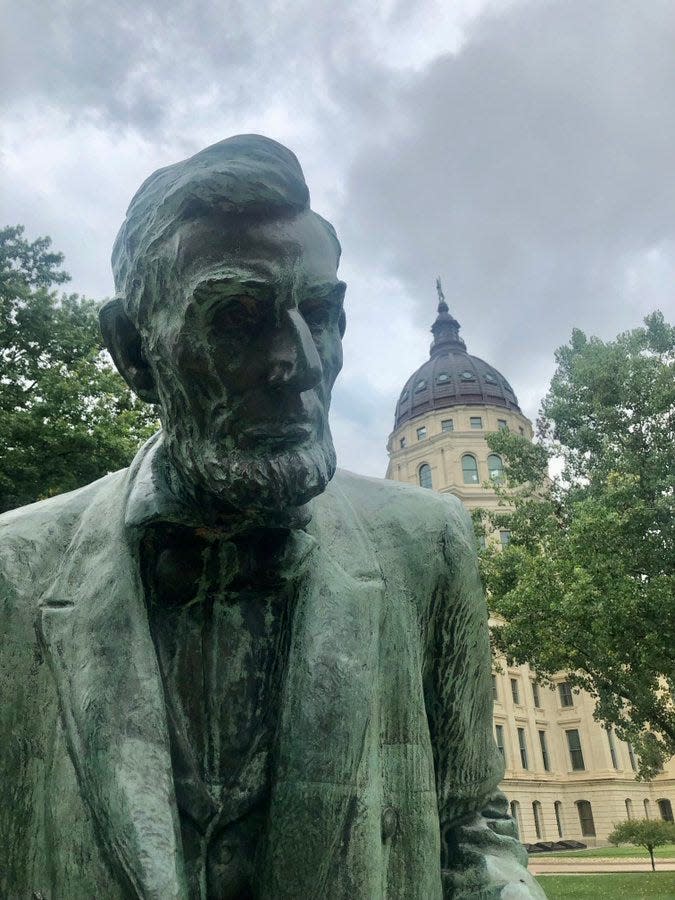 During a break from rainfall, clouds hover over the Kansas Statehouse and a nearby statue of Abraham Lincoln.