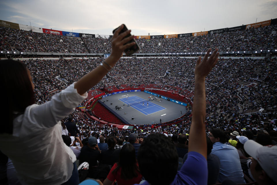 Spectators wave from the stands as brothers Bob and Mike Bryan of the U.S., left, take on Mexico's Miguel Angel Reyes Varela and Santiago Gonzalez in an exhibition doubles tennis match in the Plaza de Toros bullring in Mexico City, Saturday, Nov. 23, 2019. Roger Federer of Switzerland and Germany's Alexander Zverev were also to face off in the converted bullring Saturday, the fourth stop in a tour of Latin America by the tennis greats.(AP Photo/Rebecca Blackwell)