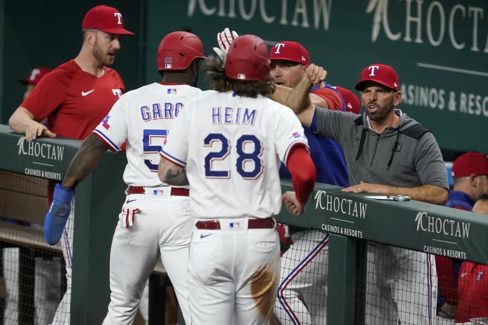 Texas Rangers' Jonah Heim (28) and Adolis Garcia, left, celebrate with manager Chris Woodward, right, and others after scoring on a Kole Calhoun single in the first inning of a baseball game against the Kansas City Royals, Tuesday, May 10, 2022, in Arlington, Texas. (AP Photo/Tony Gutierrez)
