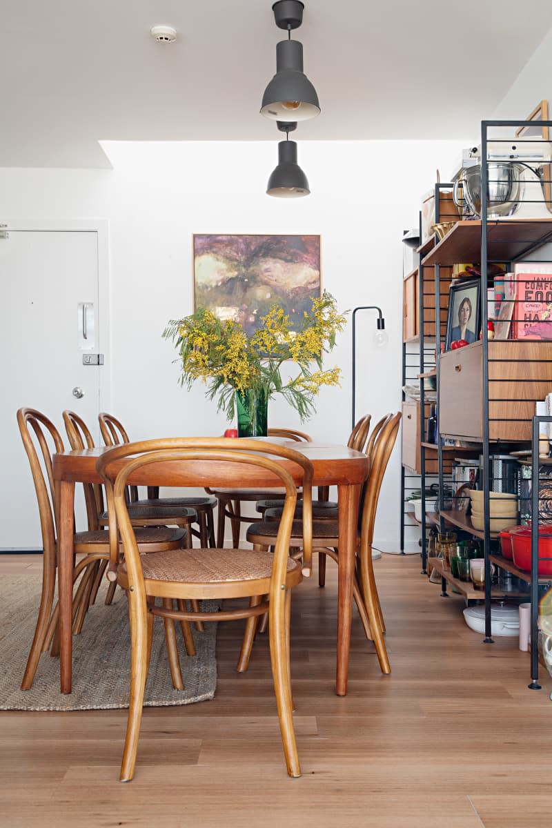 Grey industrial light fixtures hang above wooden dining table in book filled dining/kitchen area.