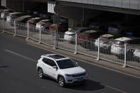 FILE - In this March 14, 2019, file photo, an SUV moves past dust-covered new Toyota cars stored underneath an overpass in Beijing. China's auto sales sank 5.4% in November from a year ago, putting the industry's biggest global market on track to shrink for a second year, an industry group reported Tues, Dec. 10, 2019. Drivers bought just over 2 million SUVs, sedans and minivans, according to the China Association of Automobile Manufacturers.(AP Photo/Andy Wong, File)