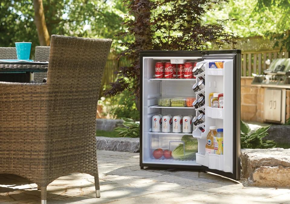 The Danby 4.4 Cu. Ft. Outdoor Fridge on an outdoor patio with its door open to reveal it's full of food.