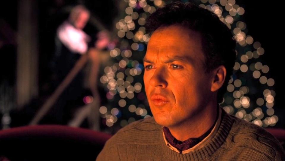 Michael Keaton's Bruce Wayne sits on the couch watching TV while Alfred decorates a Christmas tree behind him in Batman Returns