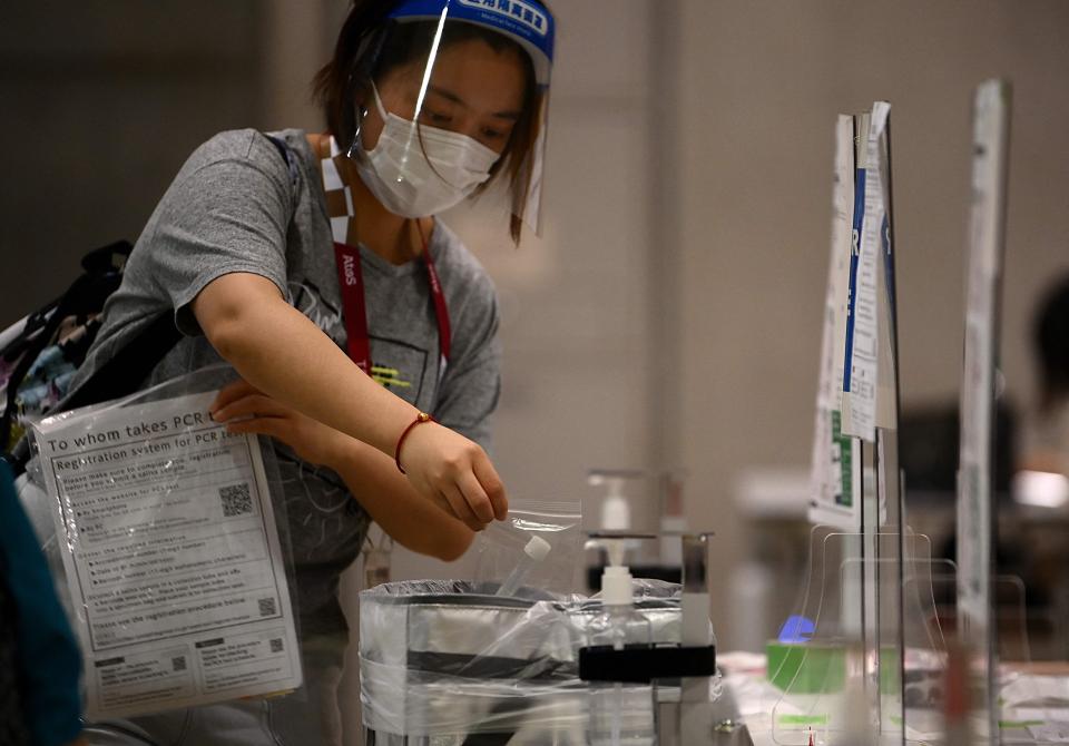 A journalist wearing a facemask as a preventive measure against the Covid-19 coronavirus drops her daily saliva sample for PCR test at the media centre ahead of the opening of the Tokyo 2020 Olympic Games in Tokyo on July 20, 2021.